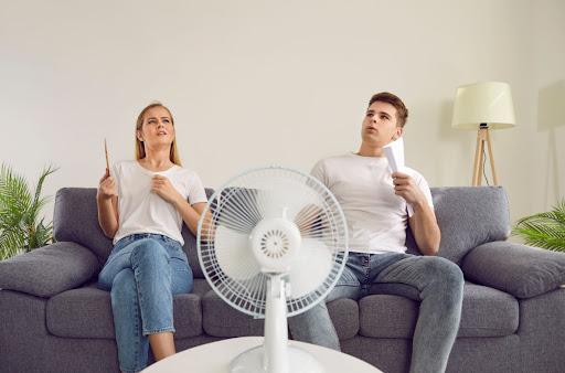 A man and woman sitting on a couch in front of a man with paper fans in their hands.